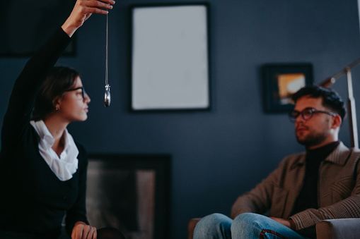 A beautiful and focused female hypnotherapist holding a pocket watch and working on one of the practice at the office with her patient, called hypnotherapy.