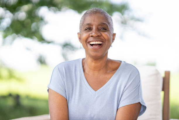 A middle aged woman of African decent, who is beating Cancer, is sitting outside on a sunny summer day as she poses for a portrait. She is dressed casually in a light blue t-shirt and is smiling with the news that she is beating Cancer.
